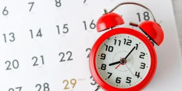 Reloj despertador rojo colocado sobre un calendario, con el número 29 resaltado.